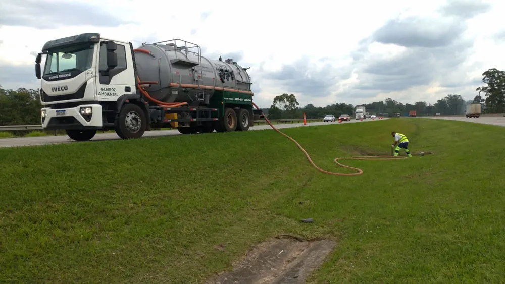 Caminhão tanque da Leiroz Ambiental em operação na beira da rodovia, com mangueira laranja no gramado
