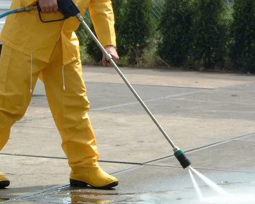 Operador com macacão amarelo fazendo hidrojateamento na grama